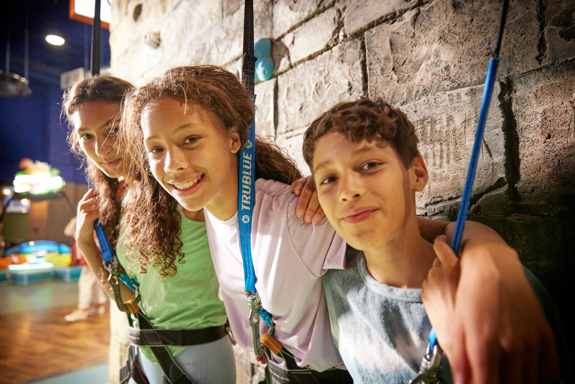 3 children smiling in front of climbing wall